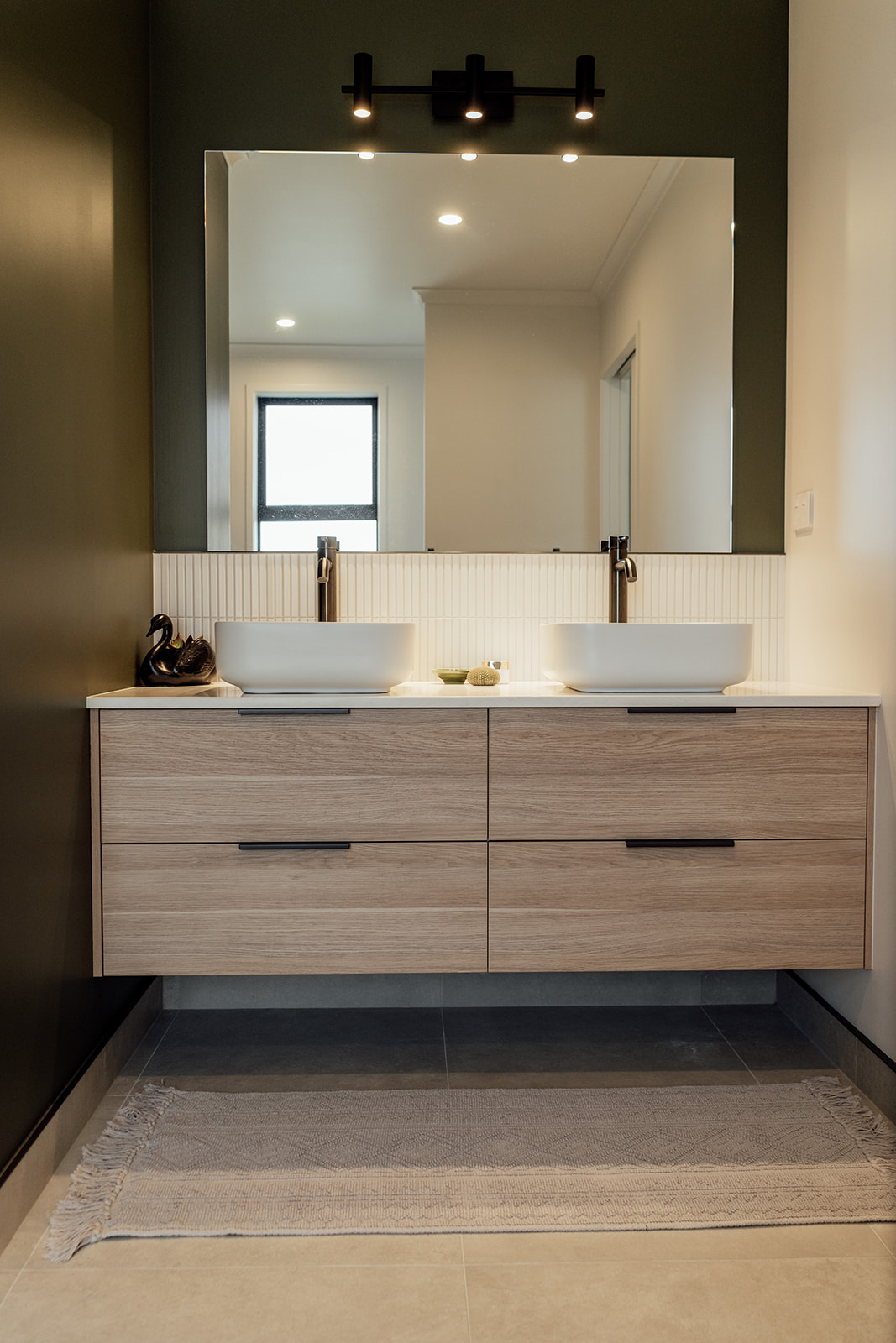 Light wood grain vanity floating off the floor with 2 top mounted basins on a slim white benchtop. Large square mirrorwith black feature lights above.